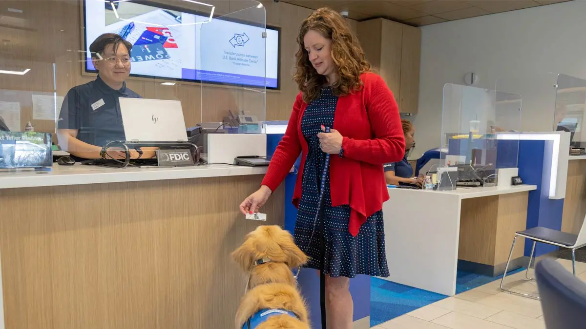 Photo of a female customer being assisted by her dog to make a transaction at a U.S. Bank branch