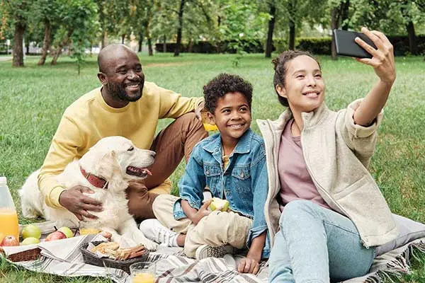 A family having a picnic outside with their dog, taking a picture of themselves