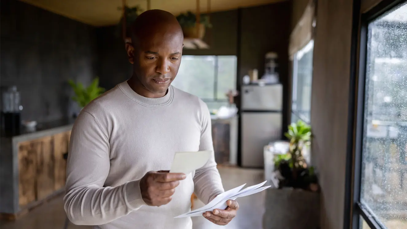 man looking at a document while holding a stack of mail