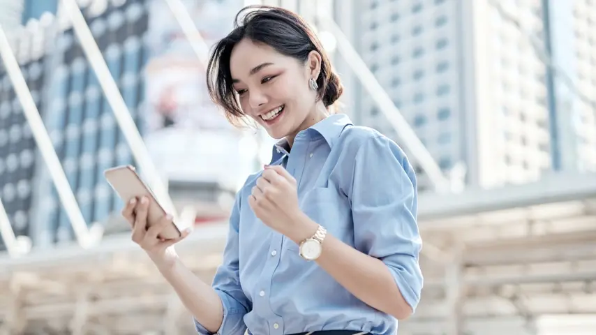 A person smiling looking at their phone outside  