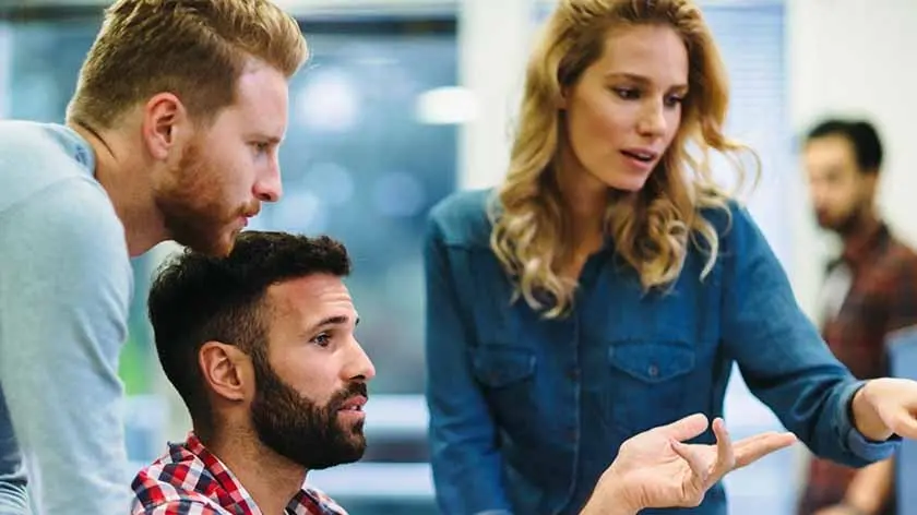Three coworkers huddled around a computer discussing how AI impacts treasury management