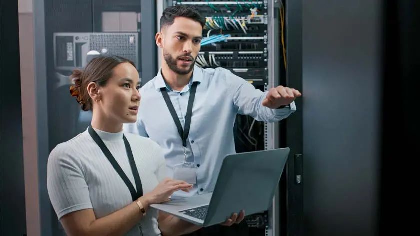 Two IT workers in a server room doing an inspection to help prevent cybersecurity fraud