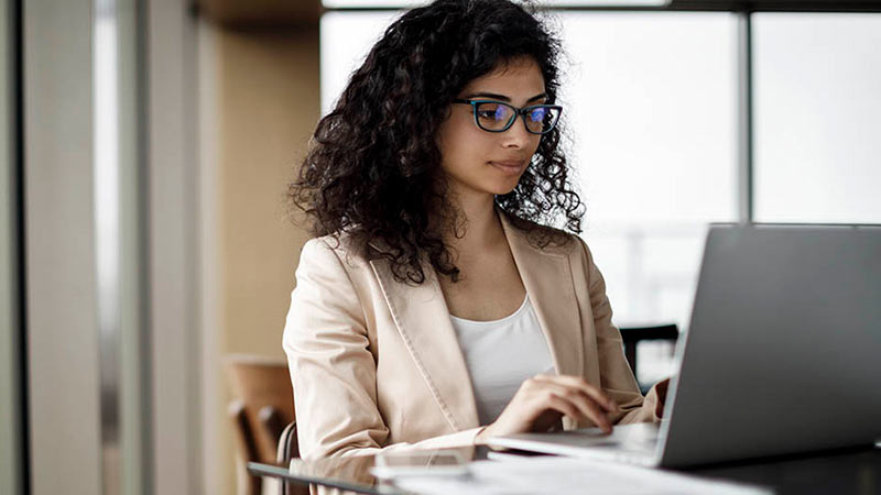 Young professional woman sitting at a laptop and reading about questions to ask custody providers
