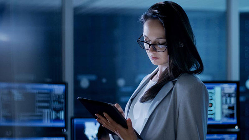 Woman standing in a room with several computers and looking at her tablet device