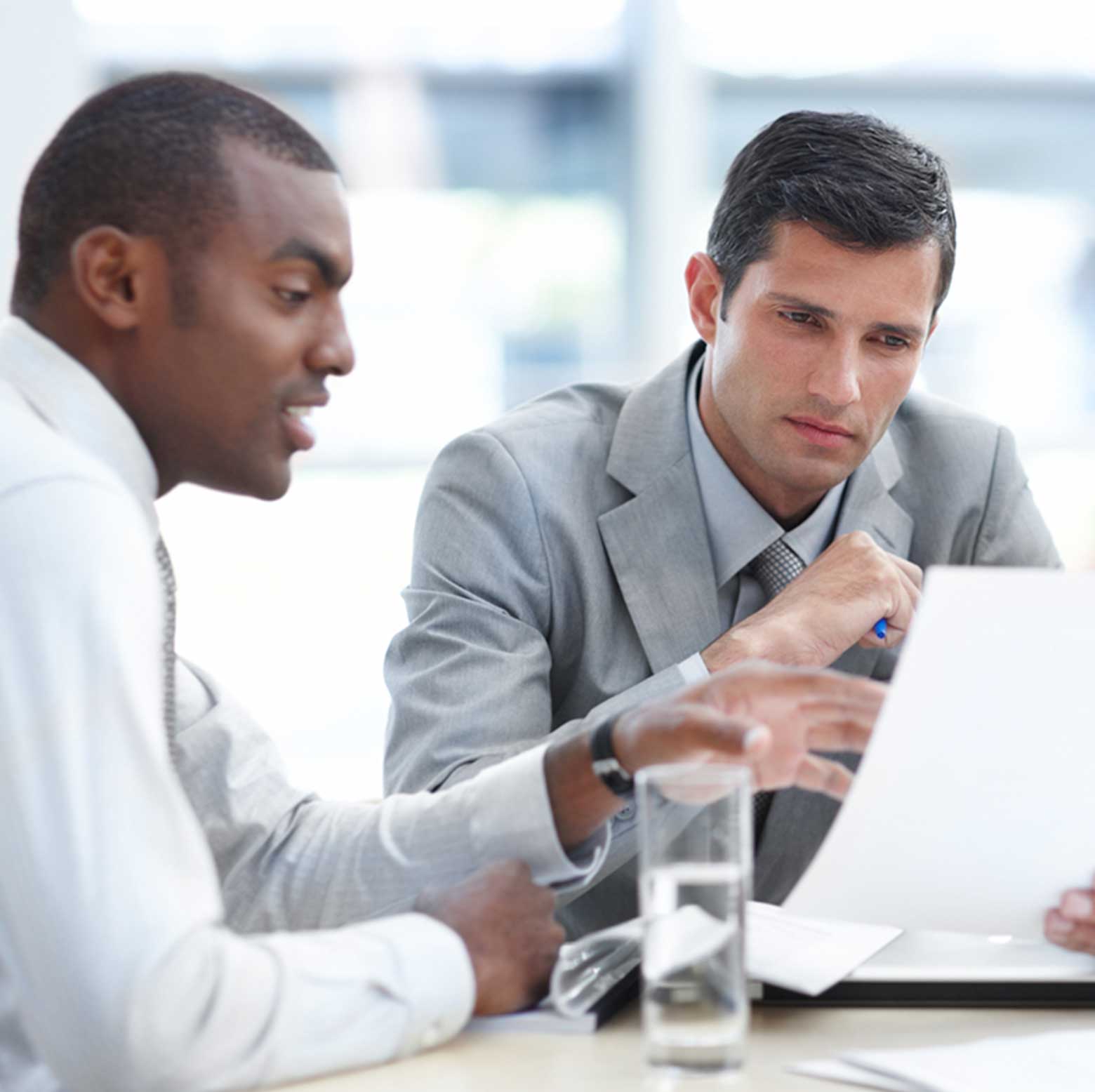 Two professional men at a table with a glass of water and looking at paper