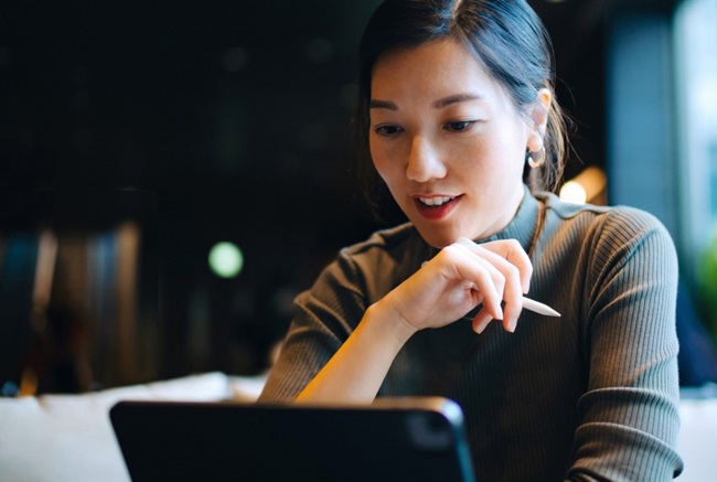 oung woman holding a pen and researching ETFs on her laptop