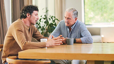 Older man and his son sitting at a kitchen table discussing wealth management