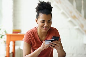 Young woman, smiling, looking down at her mobile phone and credit card