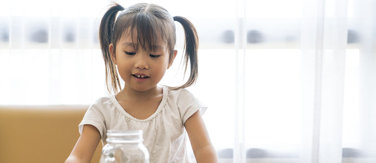 Girl smiling as she puts coins in a glass jar.
