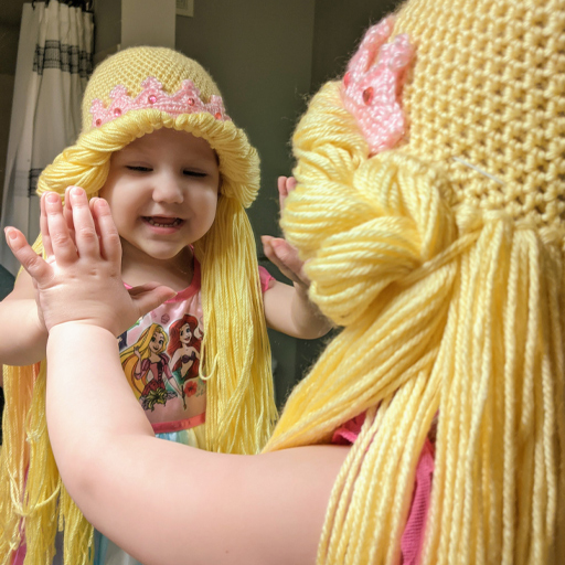 A girl wearing a yarn princess wig looking in the mirror.