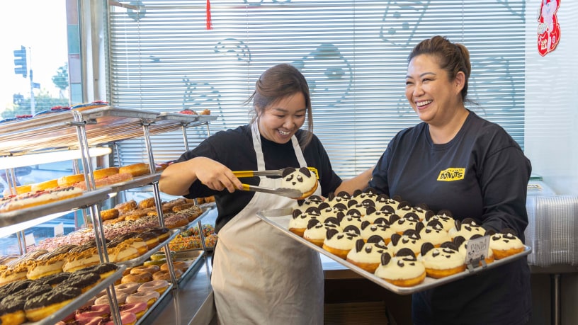 Sisters working together making custom donuts at their small business family donut shop.