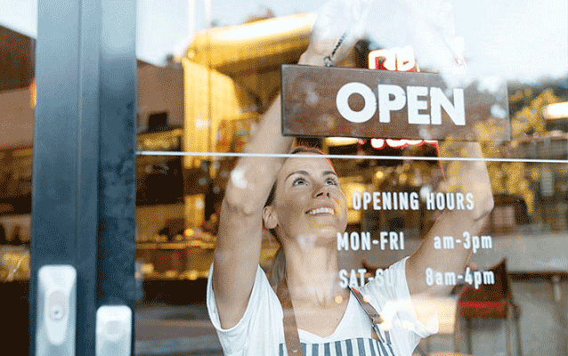 Woman hanging an “Open” sign on the door of her small business.