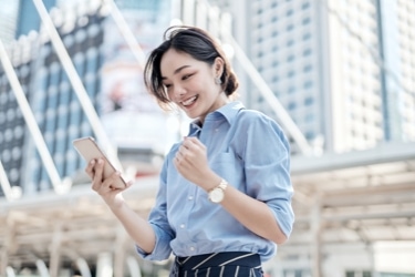 A person smiling while looking at their mobile phone outside