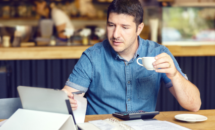 Man at a desk drinking coffee while reviewing paperwork.