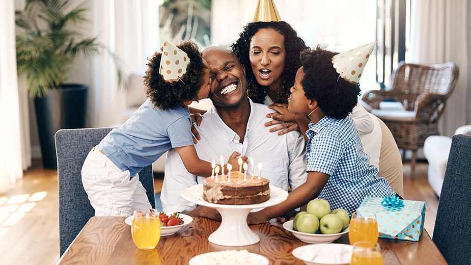 A Black family of a father, mother and two children celebrate Dad’s birthday with a birthday cake and candles