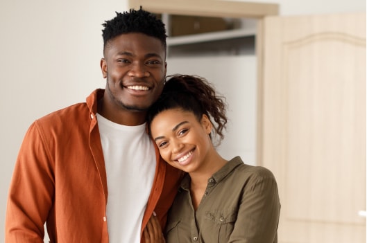A young Black couple poses happily for the camera inside their new home.