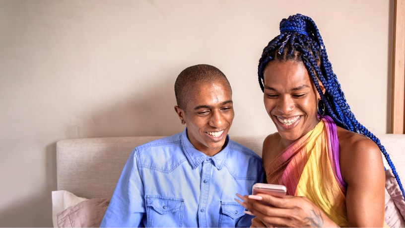 A young man and transgender woman look at a cell phone together.